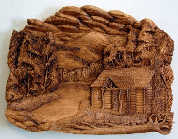 Relief carving of log cabin with mountains, trees and a lake in the background. Titled Northwoods Cabin