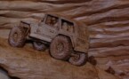 close up of a pictorial relief scene of a rock climbing jeep with mountains and clouds in the background