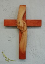 cross with the hand of Jesus grasping another hand carved by Dylan Goodson